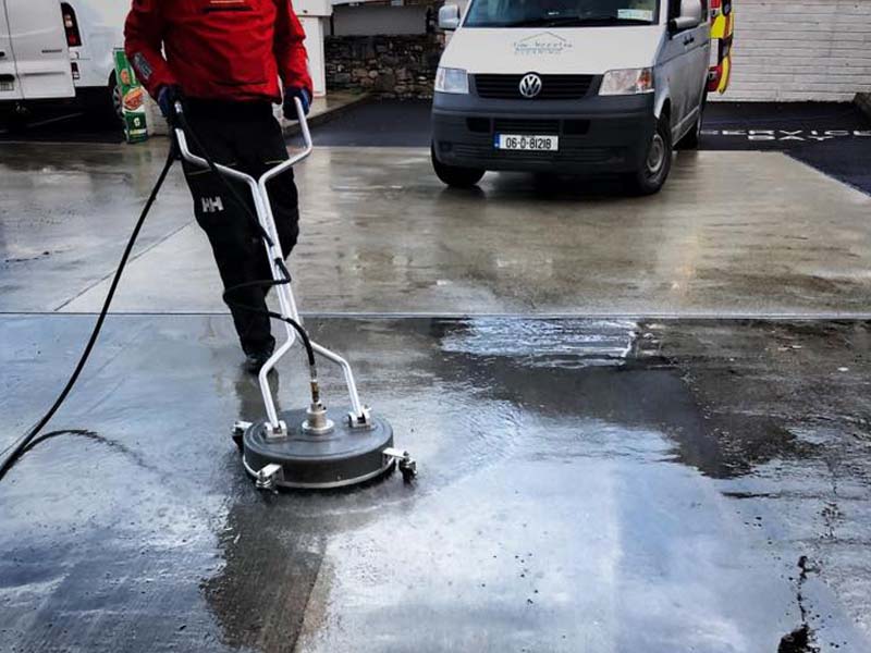 Powerwashing a driveway, cleaned section visible against dirty concrete