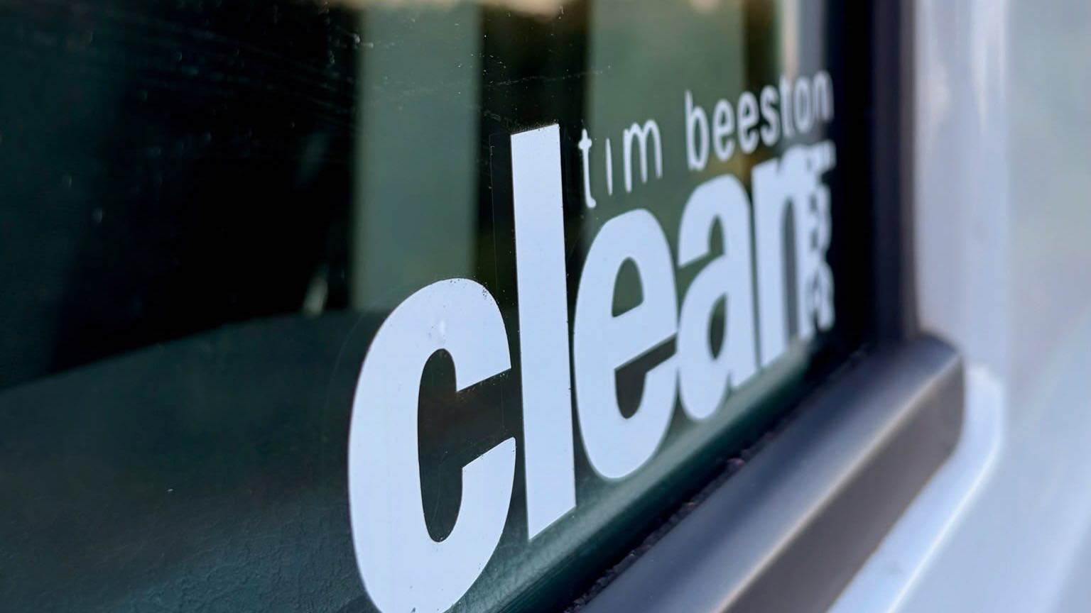 Close-up of the Tim Beeston Cleaning decal on a freshly cleaned window at sunset